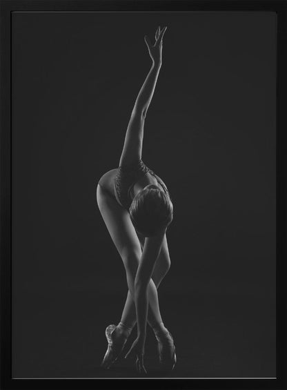 A dramatic black and white photograph of a ballerina posed against a dark background. She is bent forward at the waist, with her legs crossed and on pointe. One arm reaches up towards the ceiling in a graceful curve while the other hand touches the floor near her feet, showcasing her flexibility and strength. Wall Art
