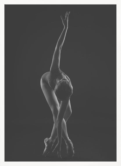 A dramatic black and white photograph of a ballerina posed against a dark background. She is bent forward at the waist, with her legs crossed and on pointe. One arm reaches up towards the ceiling in a graceful curve while the other hand touches the floor near her feet, showcasing her flexibility and strength. Wall Art