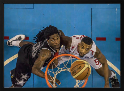An overhead, bird's-eye view photograph of two basketball players looking up from below the hoop as a basketball goes through the net. The court is bright blue, and the image is enclosed in a silver frame. Poster