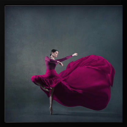 A graceful ballet dancer in a vibrant magenta dress strikes a pose on pointe, with the long, flowing fabric of her skirt billowing out dramatically behind her against a dark, textured gray background, all enclosed in a simple light wood frame. Decor