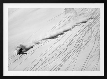 A dramatic black and white overhead photograph of a skier carving down a steep, powder-filled mountain slope, kicking up a huge plume of snow. Numerous ski tracks crisscross the pristine white snow, creating a pattern of dark lines. Poster