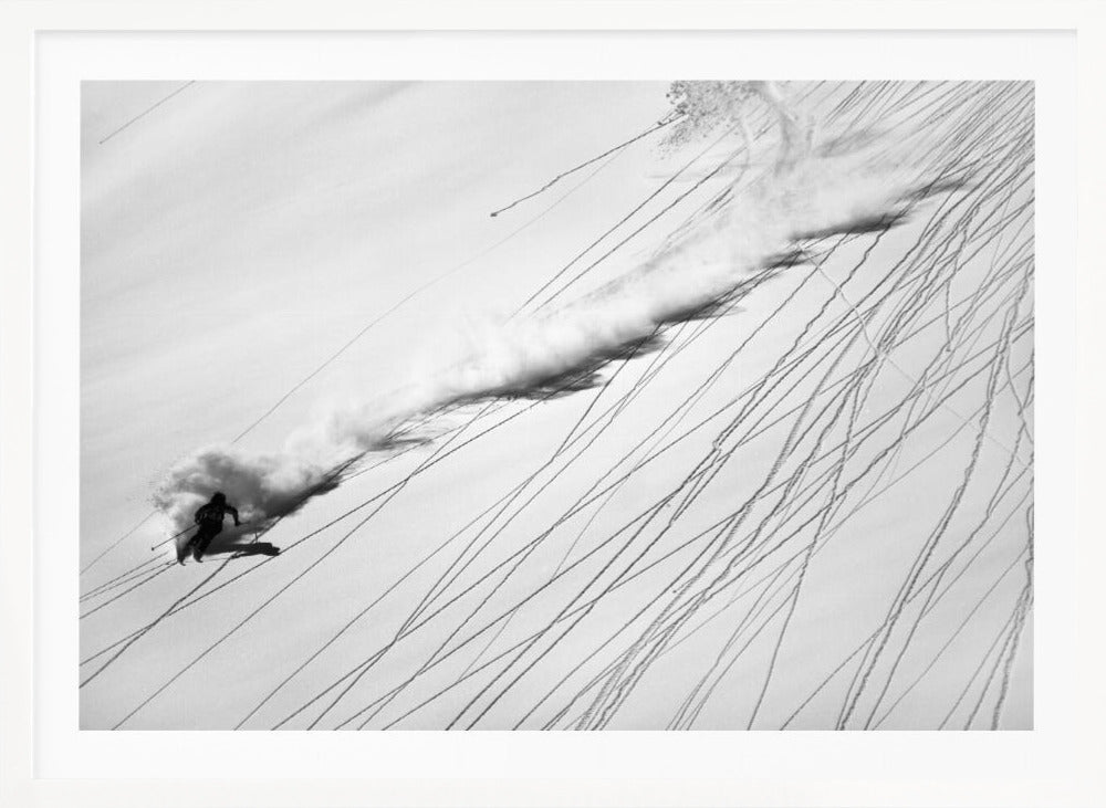 A dramatic black and white overhead photograph of a skier carving down a steep, powder-filled mountain slope, kicking up a huge plume of snow. Numerous ski tracks crisscross the pristine white snow, creating a pattern of dark lines. Poster