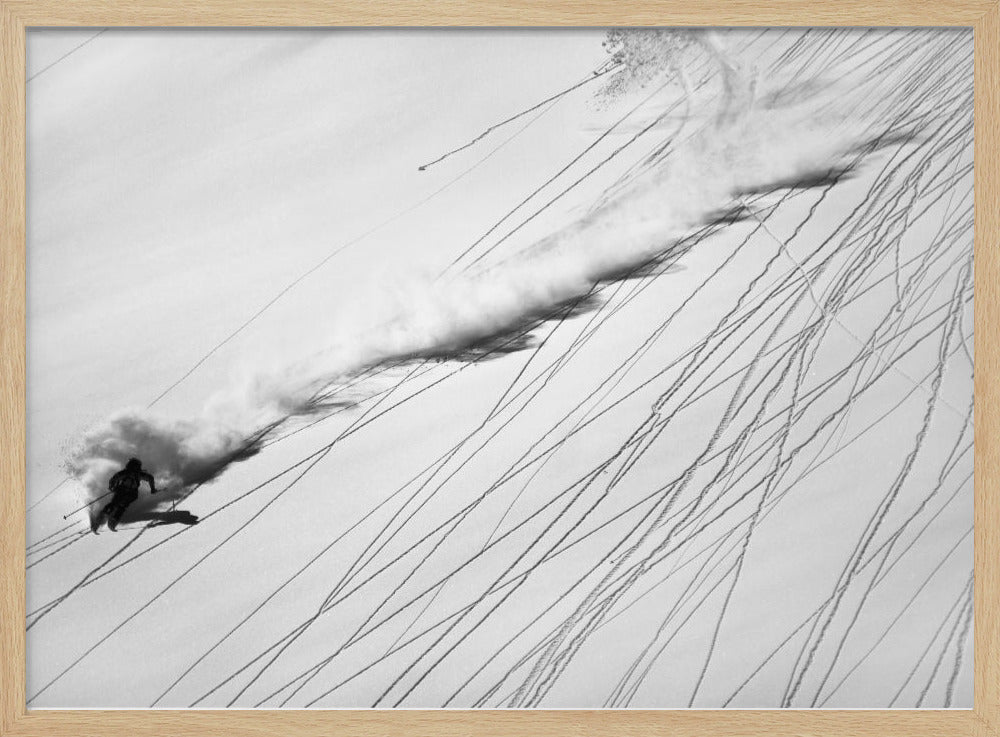 A dramatic black and white overhead photograph of a skier carving down a steep, powder-filled mountain slope, kicking up a huge plume of snow. Numerous ski tracks crisscross the pristine white snow, creating a pattern of dark lines. Poster