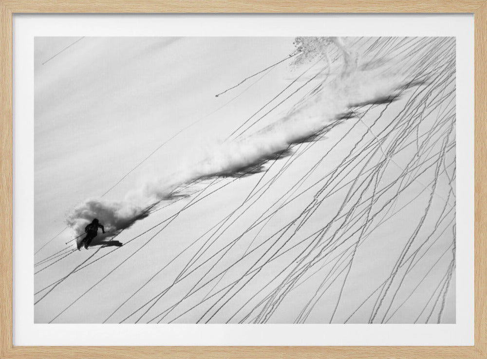 A dramatic black and white overhead photograph of a skier carving down a steep, powder-filled mountain slope, kicking up a huge plume of snow. Numerous ski tracks crisscross the pristine white snow, creating a pattern of dark lines. Poster