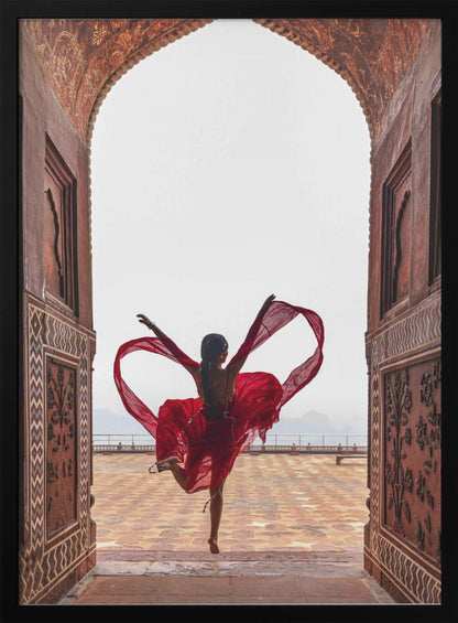A woman in a flowing red dress dances joyfully, framed by an ornate, carved archway. Seen from behind, she leaps with her arms outstretched, holding a long red scarf that forms a heart shape around her against a bright, hazy sky. Poster