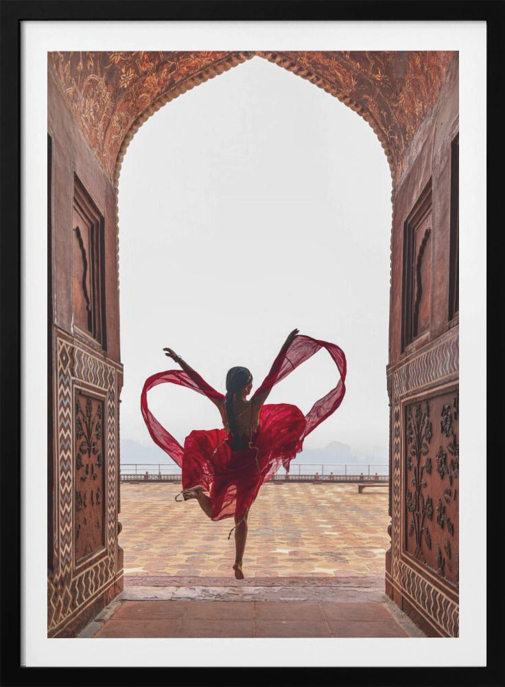 A woman in a flowing red dress dances joyfully, framed by an ornate, carved archway. Seen from behind, she leaps with her arms outstretched, holding a long red scarf that forms a heart shape around her against a bright, hazy sky. Poster