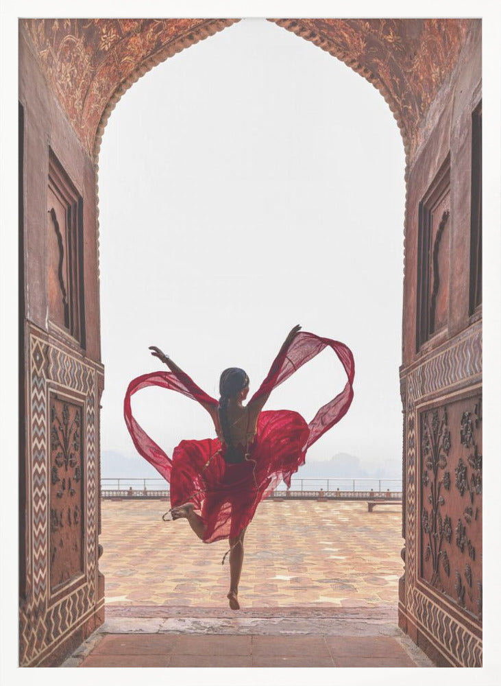 A woman in a flowing red dress dances joyfully, framed by an ornate, carved archway. Seen from behind, she leaps with her arms outstretched, holding a long red scarf that forms a heart shape around her against a bright, hazy sky. Poster
