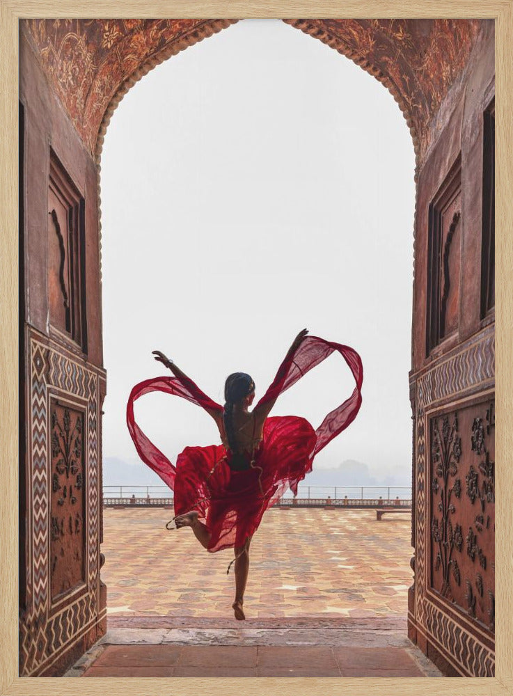A woman in a flowing red dress dances joyfully, framed by an ornate, carved archway. Seen from behind, she leaps with her arms outstretched, holding a long red scarf that forms a heart shape around her against a bright, hazy sky. Poster