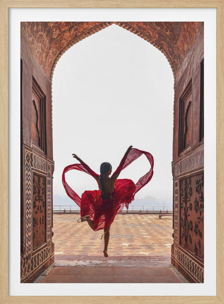A woman in a flowing red dress dances joyfully, framed by an ornate, carved archway. Seen from behind, she leaps with her arms outstretched, holding a long red scarf that forms a heart shape around her against a bright, hazy sky. Poster