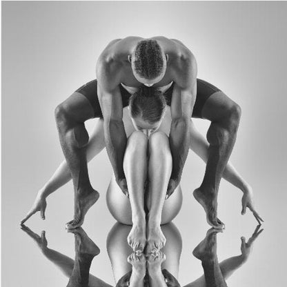 A framed black and white studio photograph of two dancers, a man and a woman, creating a symmetrical pose. The muscular man is positioned over the woman who is curled up beneath him. Their limbs are extended and reflected on the mirrored surface below, forming an abstract and powerful composition. Decor