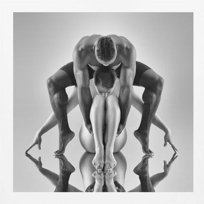 A framed black and white studio photograph of two dancers, a man and a woman, creating a symmetrical pose. The muscular man is positioned over the woman who is curled up beneath him. Their limbs are extended and reflected on the mirrored surface below, forming an abstract and powerful composition. Decor