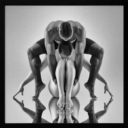 A framed black and white studio photograph of two dancers, a man and a woman, creating a symmetrical pose. The muscular man is positioned over the woman who is curled up beneath him. Their limbs are extended and reflected on the mirrored surface below, forming an abstract and powerful composition. Decor