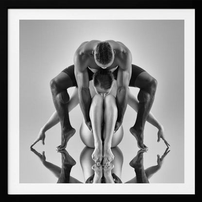 A framed black and white studio photograph of two dancers, a man and a woman, creating a symmetrical pose. The muscular man is positioned over the woman who is curled up beneath him. Their limbs are extended and reflected on the mirrored surface below, forming an abstract and powerful composition. Decor