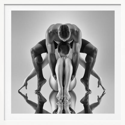 A framed black and white studio photograph of two dancers, a man and a woman, creating a symmetrical pose. The muscular man is positioned over the woman who is curled up beneath him. Their limbs are extended and reflected on the mirrored surface below, forming an abstract and powerful composition. Decor
