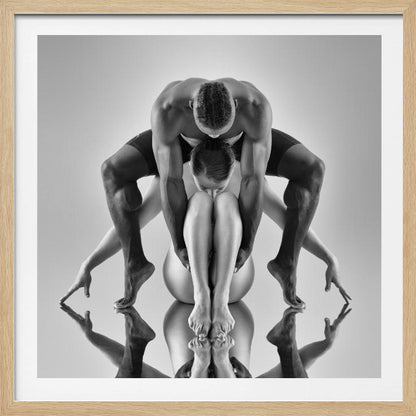 A framed black and white studio photograph of two dancers, a man and a woman, creating a symmetrical pose. The muscular man is positioned over the woman who is curled up beneath him. Their limbs are extended and reflected on the mirrored surface below, forming an abstract and powerful composition. Decor
