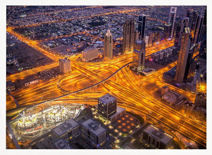 A stunning aerial view of a futuristic city at night, with brilliantly lit highways forming intricate patterns of golden light amidst towering skyscrapers, enclosed in a silver frame. Poster