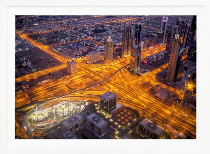 A stunning aerial view of a futuristic city at night, with brilliantly lit highways forming intricate patterns of golden light amidst towering skyscrapers, enclosed in a silver frame. Poster