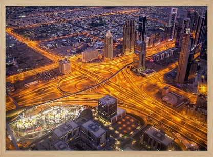 A stunning aerial view of a futuristic city at night, with brilliantly lit highways forming intricate patterns of golden light amidst towering skyscrapers, enclosed in a silver frame. Poster