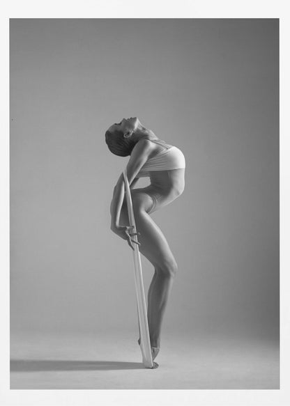 A framed black and white photograph of a graceful female dancer arching her back dramatically. She holds a long white elastic band that stretches down her body to her foot, emphasizing her athletic form and flexibility against a plain studio background. Print