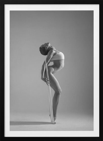 A framed black and white photograph of a graceful female dancer arching her back dramatically. She holds a long white elastic band that stretches down her body to her foot, emphasizing her athletic form and flexibility against a plain studio background. Print