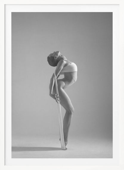 A framed black and white photograph of a graceful female dancer arching her back dramatically. She holds a long white elastic band that stretches down her body to her foot, emphasizing her athletic form and flexibility against a plain studio background. Print
