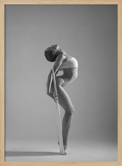 A framed black and white photograph of a graceful female dancer arching her back dramatically. She holds a long white elastic band that stretches down her body to her foot, emphasizing her athletic form and flexibility against a plain studio background. Print
