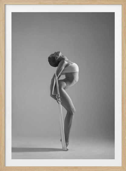 A framed black and white photograph of a graceful female dancer arching her back dramatically. She holds a long white elastic band that stretches down her body to her foot, emphasizing her athletic form and flexibility against a plain studio background. Print