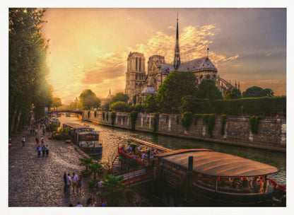 A scenic photograph of the Notre Dame Cathedral in Paris during a warm, golden sunset, as viewed from across the River Seine. People are strolling along the cobblestone riverbank and riding on tour boats docked on the water. The image is presented within a silver picture frame. Decor