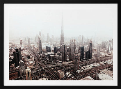 An aerial photograph of a sprawling modern cityscape on a hazy day, framed in silver. The iconic Burj Khalifa stands tall in the center background, surrounded by numerous other skyscrapers and a complex network of highways and interchanges in the foreground, all rendered in a muted, slightly sepia-toned color palette. Print
