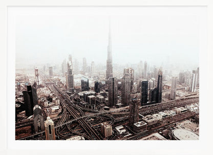 An aerial photograph of a sprawling modern cityscape on a hazy day, framed in silver. The iconic Burj Khalifa stands tall in the center background, surrounded by numerous other skyscrapers and a complex network of highways and interchanges in the foreground, all rendered in a muted, slightly sepia-toned color palette. Print