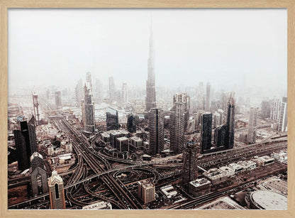 An aerial photograph of a sprawling modern cityscape on a hazy day, framed in silver. The iconic Burj Khalifa stands tall in the center background, surrounded by numerous other skyscrapers and a complex network of highways and interchanges in the foreground, all rendered in a muted, slightly sepia-toned color palette. Print