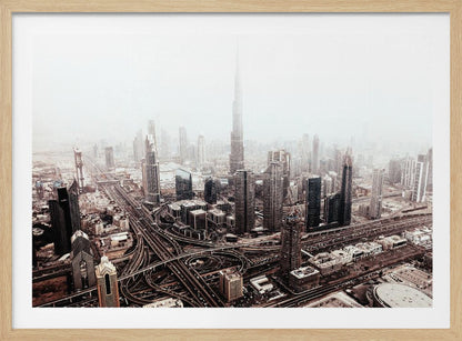 An aerial photograph of a sprawling modern cityscape on a hazy day, framed in silver. The iconic Burj Khalifa stands tall in the center background, surrounded by numerous other skyscrapers and a complex network of highways and interchanges in the foreground, all rendered in a muted, slightly sepia-toned color palette. Print