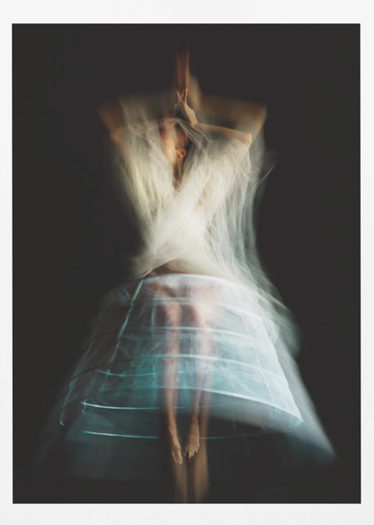 An ethereal, long-exposure photograph of a dancing figure against a dark gray background. The motion blur creates a ghostly effect, with white, gauzy fabric swirling around the upper body. The figure wears a transparent crinoline hoop skirt, revealing her legs and feet. Artwork