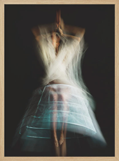 An ethereal, long-exposure photograph of a dancing figure against a dark gray background. The motion blur creates a ghostly effect, with white, gauzy fabric swirling around the upper body. The figure wears a transparent crinoline hoop skirt, revealing her legs and feet. Artwork