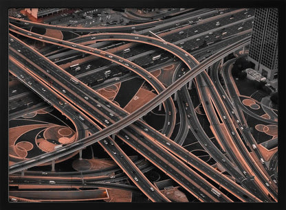 A framed aerial photograph of a sprawling, multi-level highway interchange presented in a selective color style. Dark grey roads weave over and under each other, while the surrounding land is a contrasting copper-brown, creating a dramatic and complex urban pattern. Poster