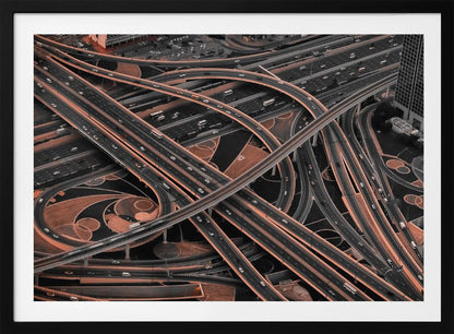 A framed aerial photograph of a sprawling, multi-level highway interchange presented in a selective color style. Dark grey roads weave over and under each other, while the surrounding land is a contrasting copper-brown, creating a dramatic and complex urban pattern. Poster