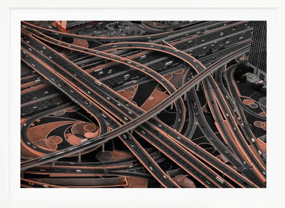 A framed aerial photograph of a sprawling, multi-level highway interchange presented in a selective color style. Dark grey roads weave over and under each other, while the surrounding land is a contrasting copper-brown, creating a dramatic and complex urban pattern. Poster