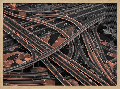 A framed aerial photograph of a sprawling, multi-level highway interchange presented in a selective color style. Dark grey roads weave over and under each other, while the surrounding land is a contrasting copper-brown, creating a dramatic and complex urban pattern. Poster