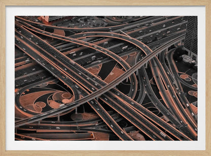 A framed aerial photograph of a sprawling, multi-level highway interchange presented in a selective color style. Dark grey roads weave over and under each other, while the surrounding land is a contrasting copper-brown, creating a dramatic and complex urban pattern. Poster