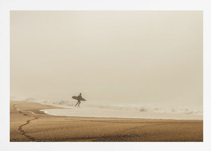 A minimalist photograph of a silhouetted surfer carrying a surfboard, running into the ocean on a foggy morning. The scene has a warm, sepia tone, with footprints visible in the wet sand in the foreground and a vast, misty sky. Wall Art