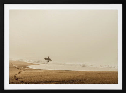 A minimalist photograph of a silhouetted surfer carrying a surfboard, running into the ocean on a foggy morning. The scene has a warm, sepia tone, with footprints visible in the wet sand in the foreground and a vast, misty sky. Wall Art