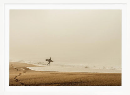 A minimalist photograph of a silhouetted surfer carrying a surfboard, running into the ocean on a foggy morning. The scene has a warm, sepia tone, with footprints visible in the wet sand in the foreground and a vast, misty sky. Wall Art
