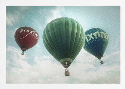 A low-angle photograph of three colorful hot air balloons floating in a cloudy blue sky, presented in a silver frame. A large green balloon is in the center, with a red balloon on the left and a dark blue balloon on the right, all featuring logos. Wall Art