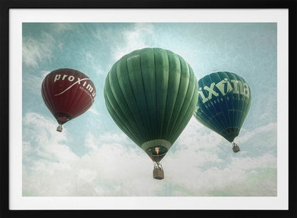 A low-angle photograph of three colorful hot air balloons floating in a cloudy blue sky, presented in a silver frame. A large green balloon is in the center, with a red balloon on the left and a dark blue balloon on the right, all featuring logos. Wall Art