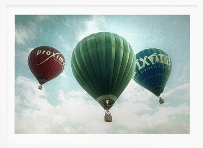 A low-angle photograph of three colorful hot air balloons floating in a cloudy blue sky, presented in a silver frame. A large green balloon is in the center, with a red balloon on the left and a dark blue balloon on the right, all featuring logos. Wall Art