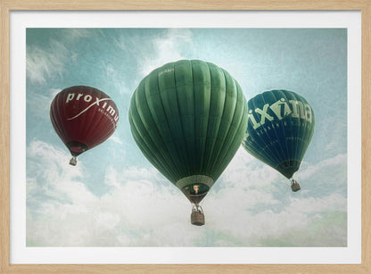A low-angle photograph of three colorful hot air balloons floating in a cloudy blue sky, presented in a silver frame. A large green balloon is in the center, with a red balloon on the left and a dark blue balloon on the right, all featuring logos. Wall Art