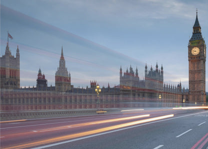 A framed, long-exposure photograph of London's Big Ben and the Houses of Parliament at dusk. In the foreground, streaks of red and yellow light from moving traffic blur across a bridge, creating a dynamic contrast with the historic architecture against a twilight sky. Decor