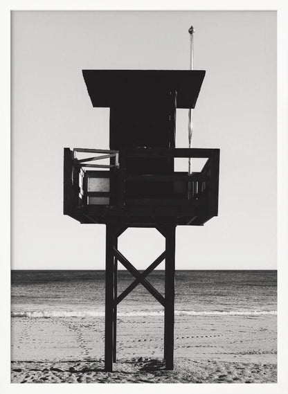 A high-contrast, black and white photograph of a silhouetted lifeguard tower standing on a sandy beach. The tower is centrally framed against a bright, empty sky, with the ocean and horizon visible in the background. Wall Art