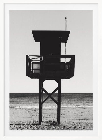 A high-contrast, black and white photograph of a silhouetted lifeguard tower standing on a sandy beach. The tower is centrally framed against a bright, empty sky, with the ocean and horizon visible in the background. Wall Art
