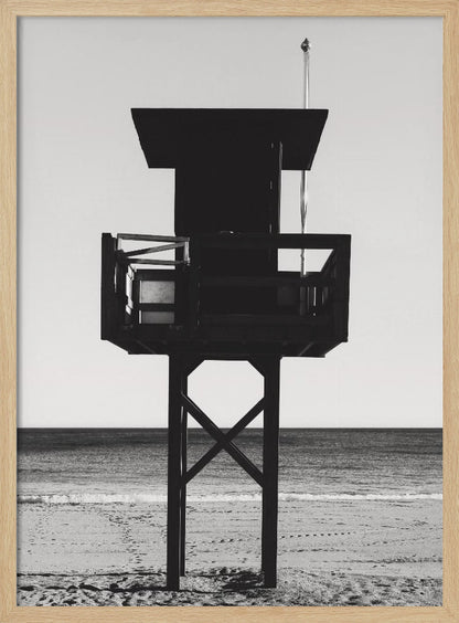 A high-contrast, black and white photograph of a silhouetted lifeguard tower standing on a sandy beach. The tower is centrally framed against a bright, empty sky, with the ocean and horizon visible in the background. Wall Art